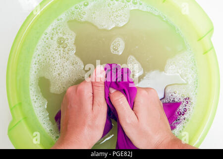 Photo on top of girl hands washing violet clothes in green basin with foam water Stock Photo