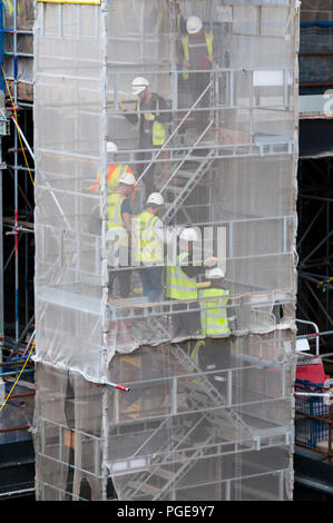 Construction workers descending a temporary staircase behind scaffold sheeting. Stock Photo