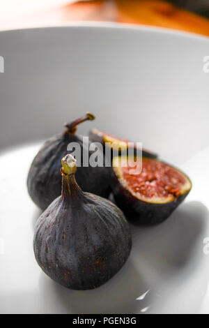 Black mission figs (including one cut in half) on a white plate Stock Photo