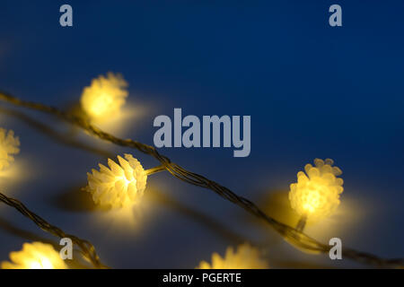 Blurred yellow christmas lights in shape of cones in three rows on dark background , low depth of focus. Stock Photo