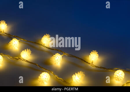 Blurred yellow christmas lights in shape of cones in three rows on dark background , low depth of focus. Stock Photo
