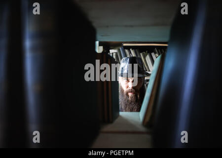 Bearded man spying through bookshelves. mystery сoncept Stock Photo