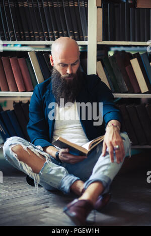 Handsome bearded man sitting on floor, reading book and relaxing in library or bookstore Stock Photo