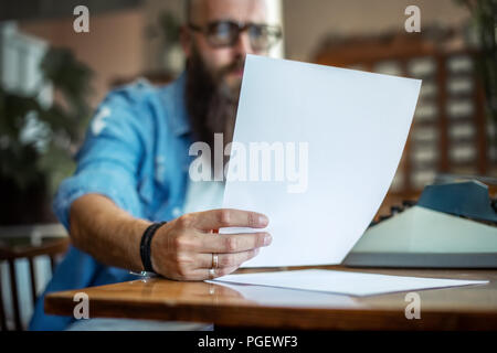 Bearded stylish writer reading his novel. Modern writer in glasses working on new book in library Stock Photo