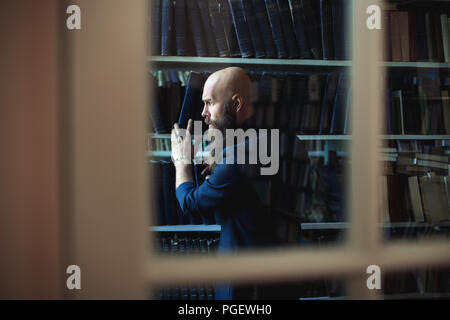 Bearded man taking book from bookshelf through window of library. Education concept Stock Photo