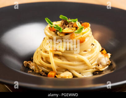 Gourmet appetizer with Italian linguine pasta in a creamy sauce, clams and truffles in a close up side view in a dark ceramic bowl Stock Photo