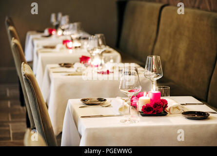 Romantic table settings in a restaurant with centrepieces of burning candles and red roses and elegant glassware for an intimate dinner for two Stock Photo