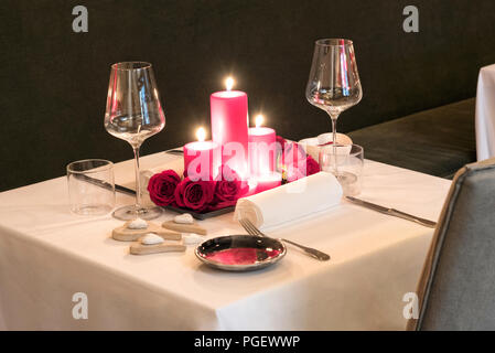 Romantic candlelit table setting for two with a centrepiece of burning red candles and fresh flowers set with matching red dinnerware and elegant glas Stock Photo