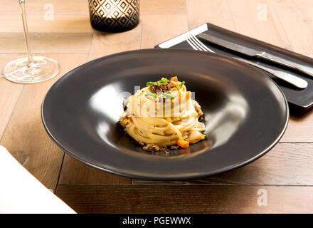 Gourmet seafood appetizer of Italian linguine pasta, truffle and clams served in a dark ceramic dish on a simple wooden table setting Stock Photo