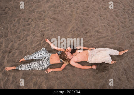 aerial view picture of young cheerful beautiful couple laying down at the beach on the sand. relax and enjoy the summer season in holiday. ethnic and  Stock Photo