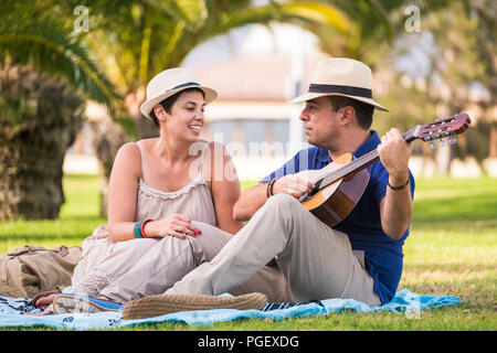 nice happy alternative couple enjoy the outdoor leisure activity together with love and fun playing an acoustic guitar and singing some songs. sitting Stock Photo