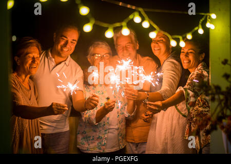 group of people celebrate an event like new years eve or birthday all together with sparkles light by night in the dark. smiles and having fun in frie Stock Photo