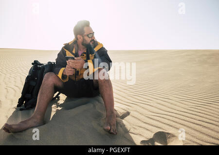 lonely caucasian middle age man travel barefoot in the desrt with backpack and phone and tripod to take pictures. alternative travel vacation concept  Stock Photo