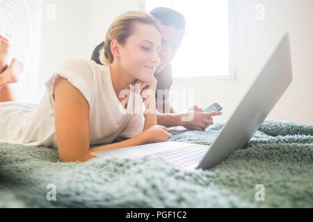 nice caucasian young attractive couple stay lay down on the bed working with laptop and mobile phone internet connected. indoor home leisure activity 