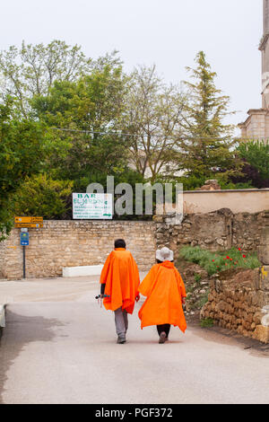 Two pilgrims wearing orange wet weather poncho capes walking into the town of Castrojeriz  while walking the Camino de Santiago the way of St James Stock Photo