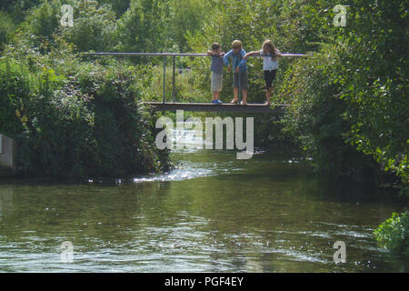 Three young children stand on a bridge looking into a river in England on a summer's day Stock Photo