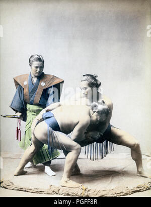 [ c. 1890s Japan - Sumo Wrestlers and Umpire ] —   Studio photograph of two rikishi (sumo wrestlers). In reality, the umpire would be wearing an eboshi (traditional black hat).  Albumen photograph published in 'Japan, Described and Illustrated by the Japanese', Shogun Edition edited by Captain F Brinkley. Published in 1897 by J B Millet Company, Boston Massachusetts, USA.  19th century vintage albumen photograph. Stock Photo