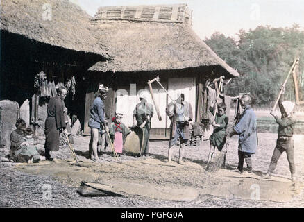 [ c. 1890s Japan - Japanese Farmers Threshing Rice ] —   Farmers threshing rice in front of traditional farm buildings.  Original text: 'Farmers threshing rice.'  Albumen photograph by Nobukuni Enami, 1890s, published in 'Japan, Described and Illustrated by the Japanese', Shogun Edition edited by Captain F Brinkley. Published in 1897 by J B Millet Company, Boston Massachusetts, USA.  19th century vintage albumen photograph. Stock Photo