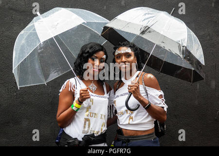 London, UK. 26 August 2018. Two young women holding umbrellas during heavy rain at Notting Hill Carnival. Photo: Bettina Strenske/Alamy Live News Stock Photo