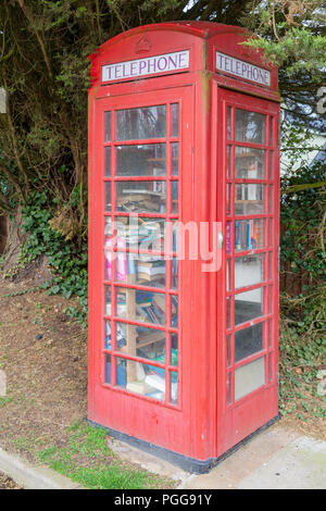 Red public telephone box in the UK. Phone booth full of books acting as a local mini library. Red phone boxes are very iconic in England and have been Stock Photo