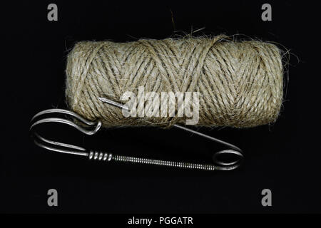 Brown rope spool with old, rusty and vintage metal safety pin on black background surface Stock Photo