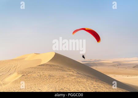 Unrecognizable paraglider flying over sand dunes in Qatar desert Stock Photo