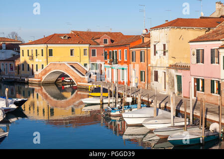 Colourful houses reflected in a tranquil canal, Murano Island, Venice, Veneto, Italy during  a blue sky winter sunset with moored boats and bridge Stock Photo