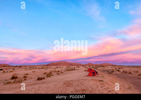 Camping in the Sahara Desert in Morocco. A row of little red tents under a colorful sunrise. Adventure travel theme.
