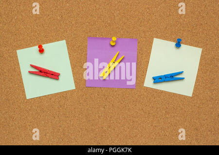 Three colorful notes with pushpins and clothespins isolated on a cork background Stock Photo