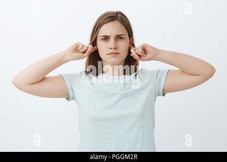 Girl not going listen shutting up ears. Intense serious-looking bothered woman covering hearing with index fingers and standing indifferent and uninvolved at camera unwilling continue conversation Stock Photo