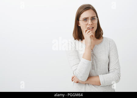 Waist-up shot of concerned troubled cute european female in glasses and blouse holding finger on lip frowning looking nervous and worried waiting for news from hospital holding hand crossed on body Stock Photo