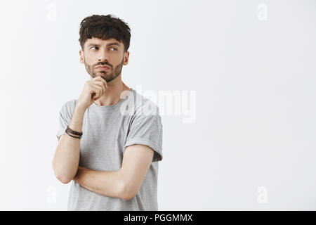 Waist-up shot of creative thoughtful intrigued good-looking guy with beard holding hand on chin turning right and gazing while thinking being curious and interested in curious scene Stock Photo