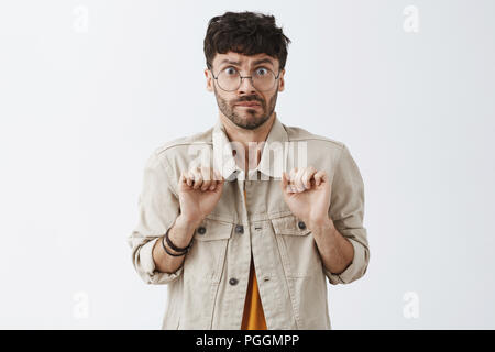 Good-looking picky and mannered caucasian bearded guy frowning, feeling disgust and being intense seeing somethign unpleasant and dirty clenching fingers from dislike over gray wall Stock Photo