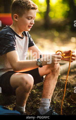 Boy tying knots in rope Stock Photo