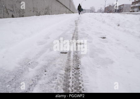 First snow of the year. A bike tire tracks in the snow on the sidewalk after a snowfall. Someone is walking far in the background. Stock Photo
