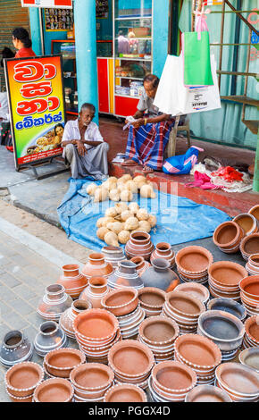 Local man selling coconuts and ceramics displayed outside on the pavement in the local Saturday coastal market at Dikwella, southern Sri Lanka Stock Photo