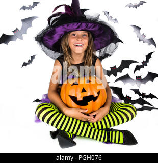 Happy halloween witch & happy pumpkin. Little girl with a halloween costume of a witch with hat, striped legs holding two smiley halloween pumpkins Stock Photo