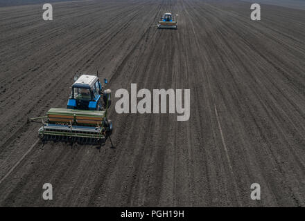 Two bright blue tractor plowing the ground against a black earth background. Stock Photo