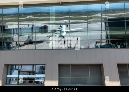 Reflection of passenger jet airplane in glass windows of airport terminal building where other passengers are waiting to board their flights Stock Photo