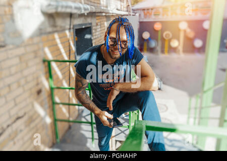 Young man with blue dreadlocks standing on green stairs. Man is on focus and foreground, green stairs is on background and blurred. Stock Photo