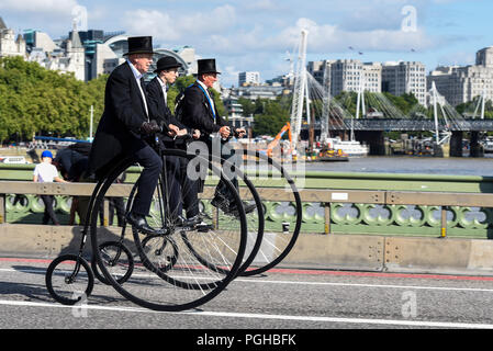 Three penny farthing cyclists ride across Westminster Bridge, London, UK. Gentlemen riders. Penny farthings by UDC, unicycle dot com. Top hats Stock Photo