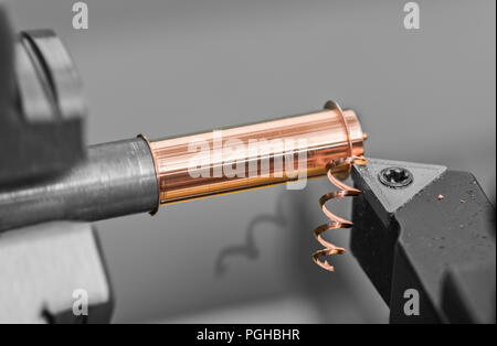 Tool bit detail working on lathe. Close-up of bronze workpiece clamped in machine chuck. Cutting tool. Twisted swarf shadow on black-white background. Stock Photo