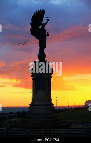 The peace statue on Brighton seafront the angel of peace silhoutted by a stunning blue red and orange sunset sky with a seagull flying past it the sea Stock Photo