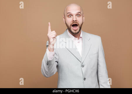 I have idea. Portrait of handsome amazed middle aged bald bearded businessman in classic gray suit standing with finger up and looking at camera with 