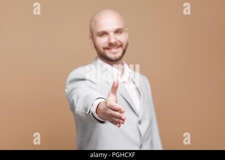 Nice to meet you. happy toothy smiling handsome middle aged bald bearded businessman in classic gray suit standing and giving handshake. indoor studio Stock Photo