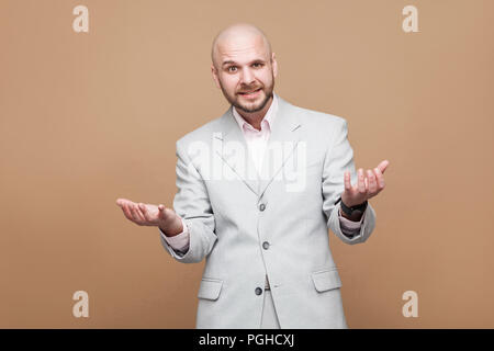 What do you want? handsome confused middle aged bearded businessman in classic light gray suit standing and looking at camera with raised arms and ask Stock Photo