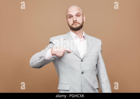 Yes I am. serious proud handsome middle aged bald bearded businessman in classic light gray suit standing looking at camera, pointing himself and prou Stock Photo