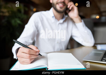 Close up of male hand holding pen over open notebook while working in cafe, copy space Stock Photo