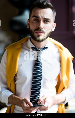 Portrait of handsome businessman looking at camera with serious face expression and holding smartphone Stock Photo