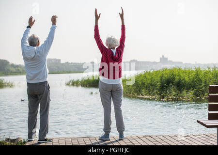 Full length back view portrait of active senior couple doing warm up exercises while standing on running track outdoors, copy space Stock Photo